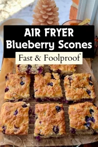 Batch of freshly baked, square blueberry scones on parchment paper, positioned beside a white candle and a full coffee mug.