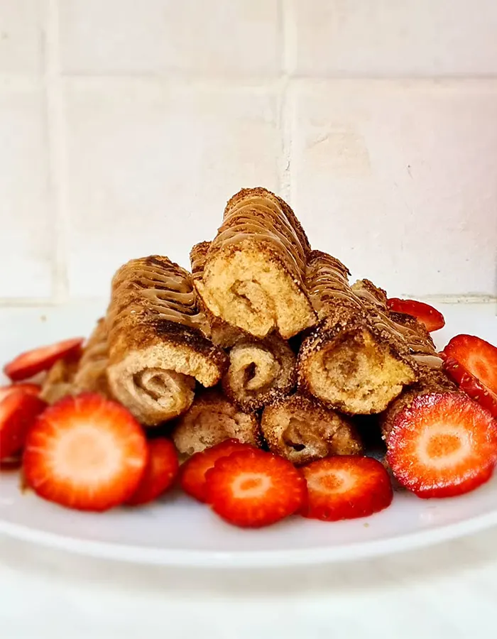Stack of cinnamon-sugar coated French toast roll ups drizzled with chocolate hazelnut spread and served with fresh sliced strawberries